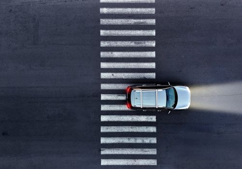 An aerial view of a silver car on a zebra crossing, its high beams are on