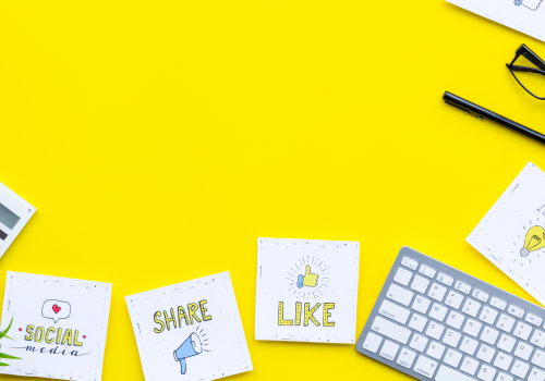 A yellow background with scattered notes saying' 'like, share', a keyboard and glasses.